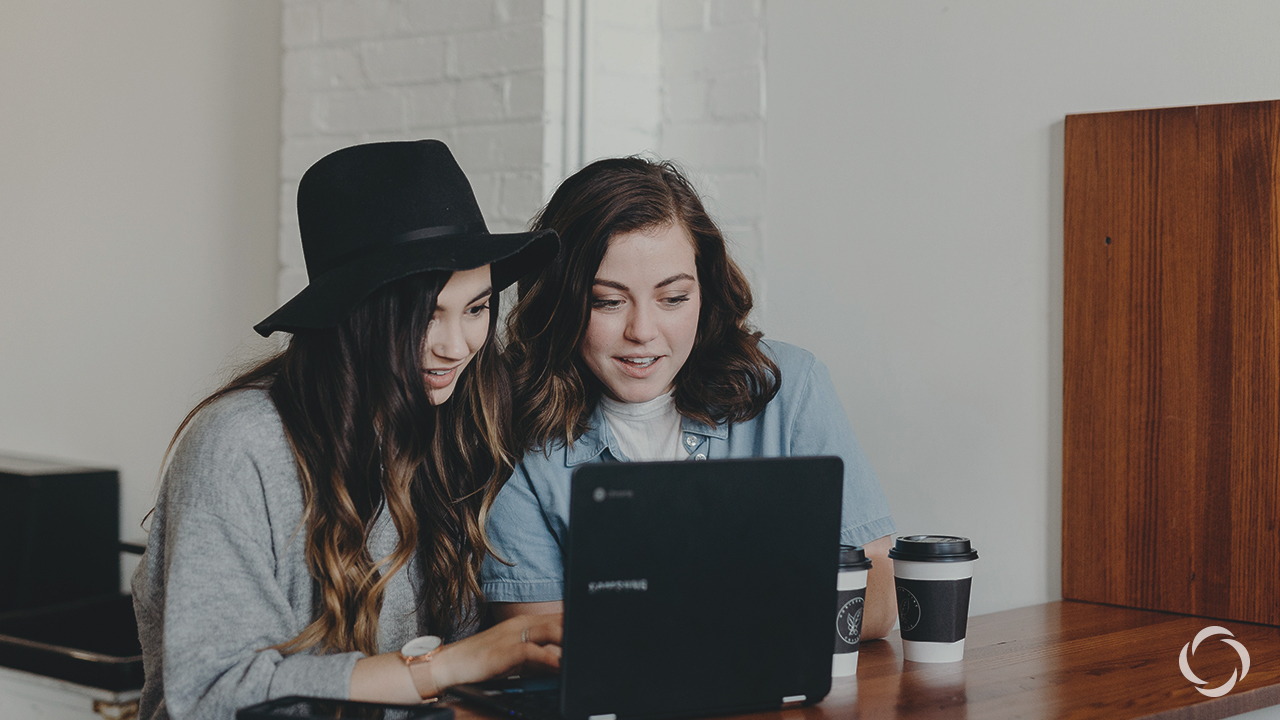 Two women with coffee looking at a computer